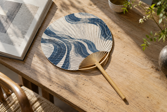 A contemporary paper hand fan with an indigo pattern on a wooden table.